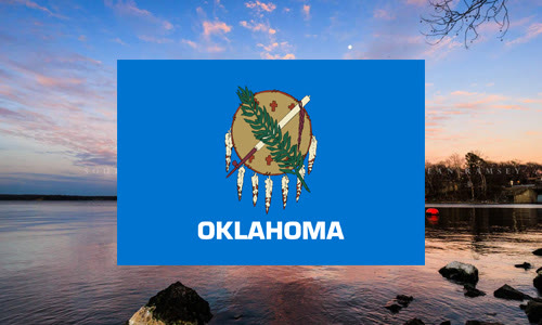Oklahoma state flag over a lake shoreline at dusk